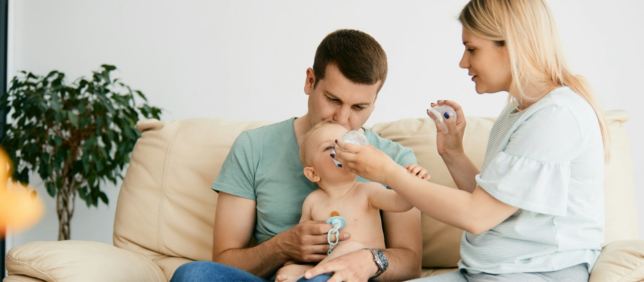 mother and father bottlefeeding a baby sitting on coach